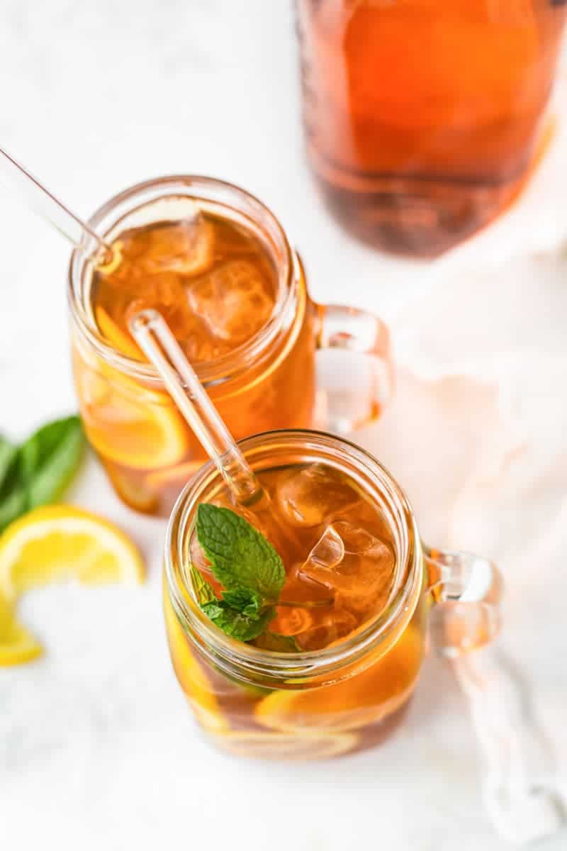 Close view of brewed sun tea over ice with mint garnish and glass straw.