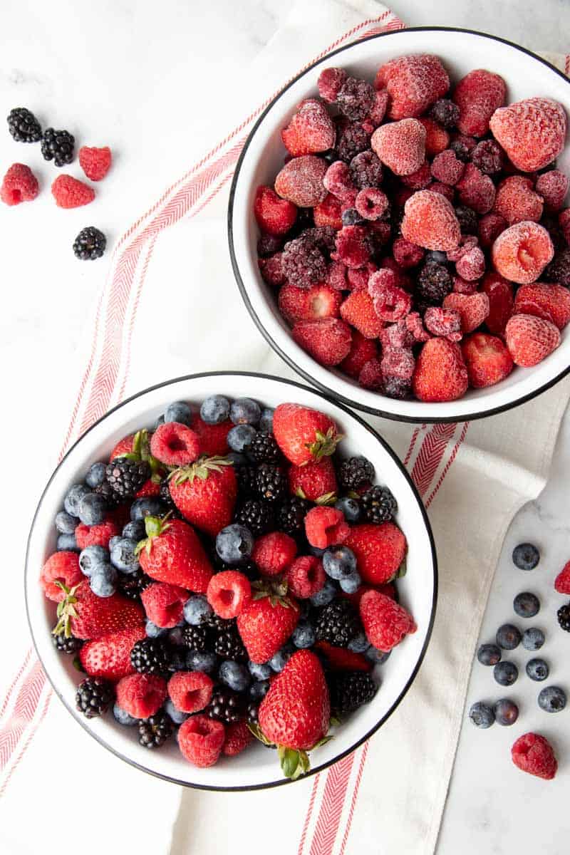 Close-up of two bowls filled with fresh and frozen mixed berries.