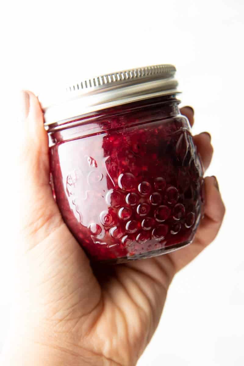 Close-up of a hand holding a full jar of mixed berry agave jam.
