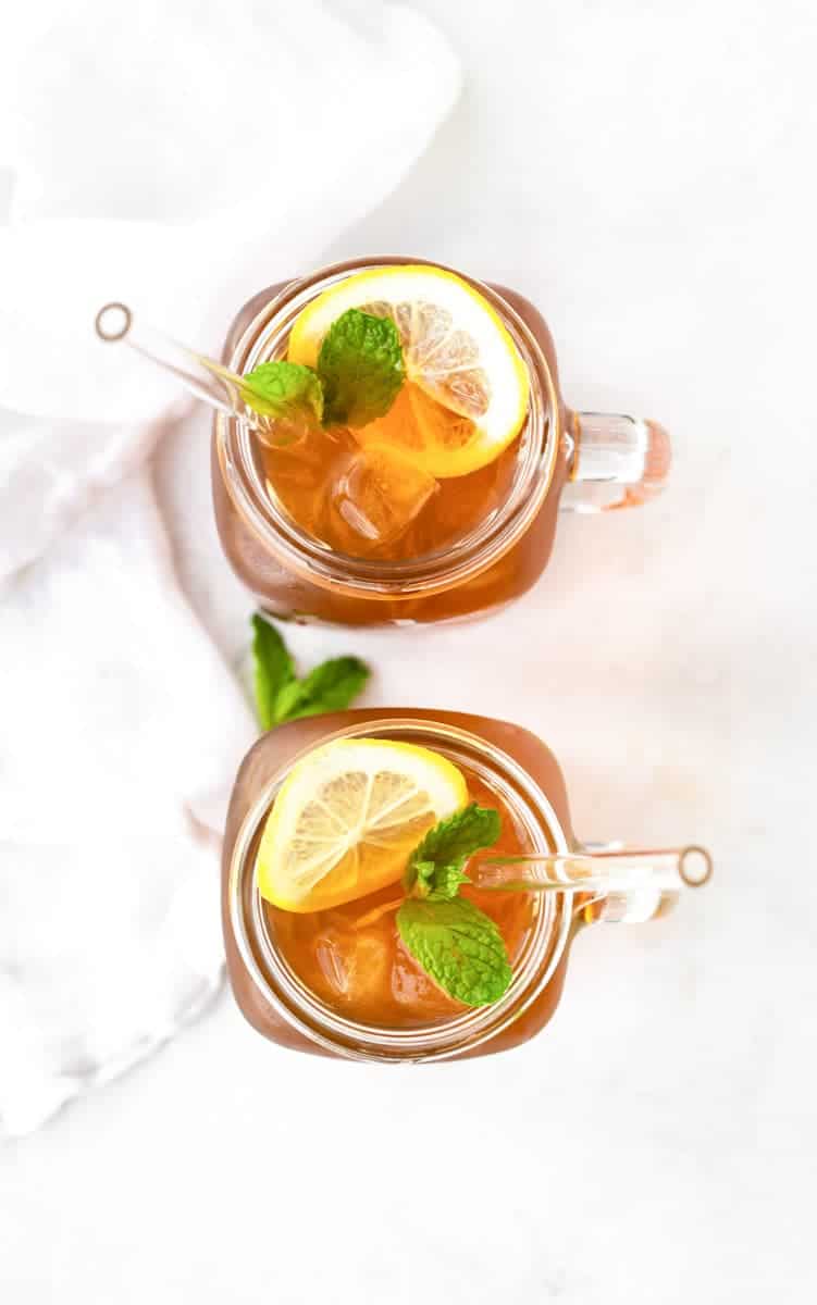 Overhead of two glasses of sun tea garnished with lemons and mint.