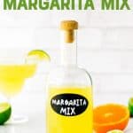 Homemade margarita mix in a glass bottle surrounded by fresh cut limes and oranges. A text overlay reads, "Homemade Margarita Mix."