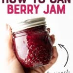 Close-up of a hand holding a full jar of mixed berry agave jam. A text overlay reads "Step-by-Step How to Can Berry Jam."