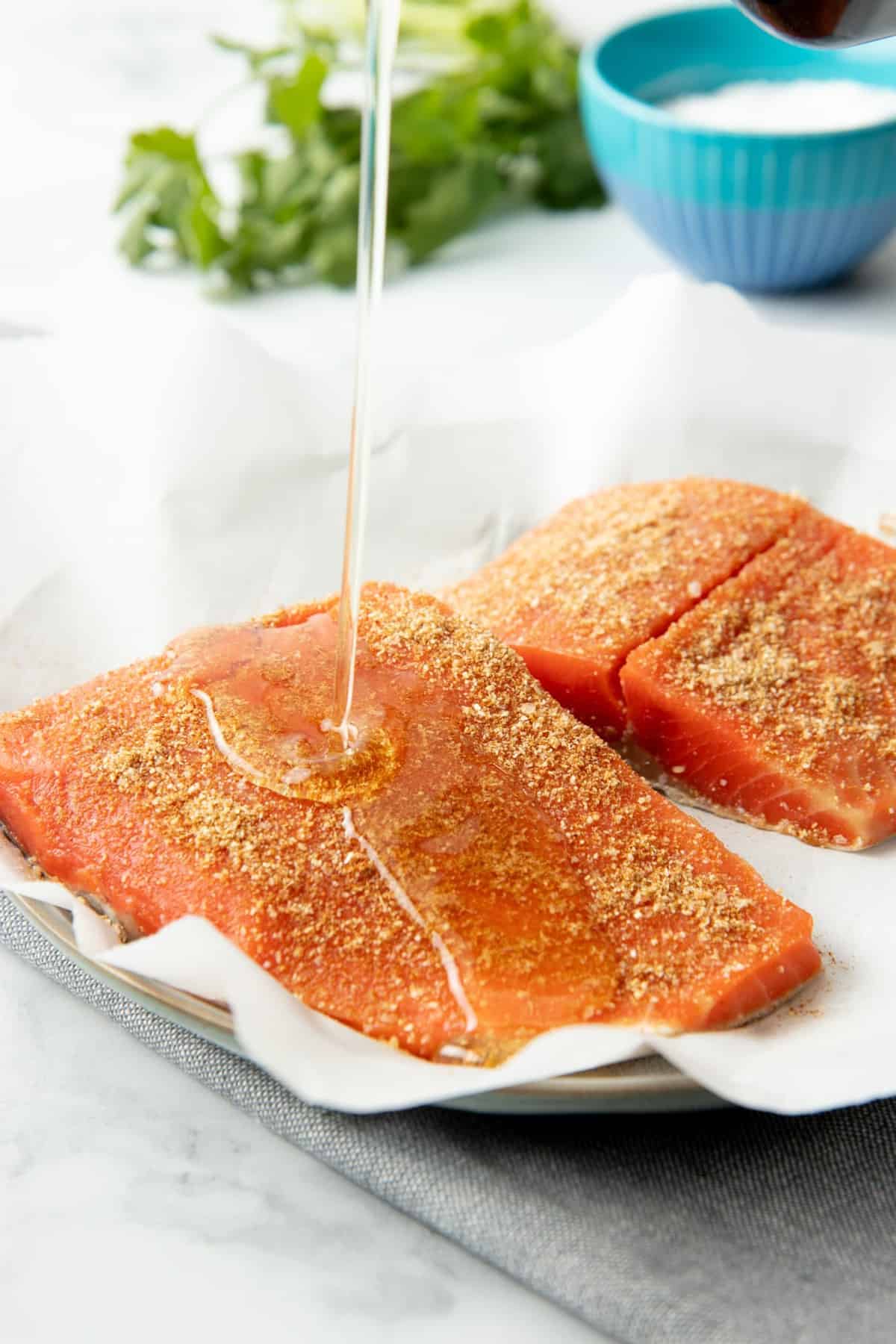 Close-up of oil pouring onto two seasoned salmon fillets.
