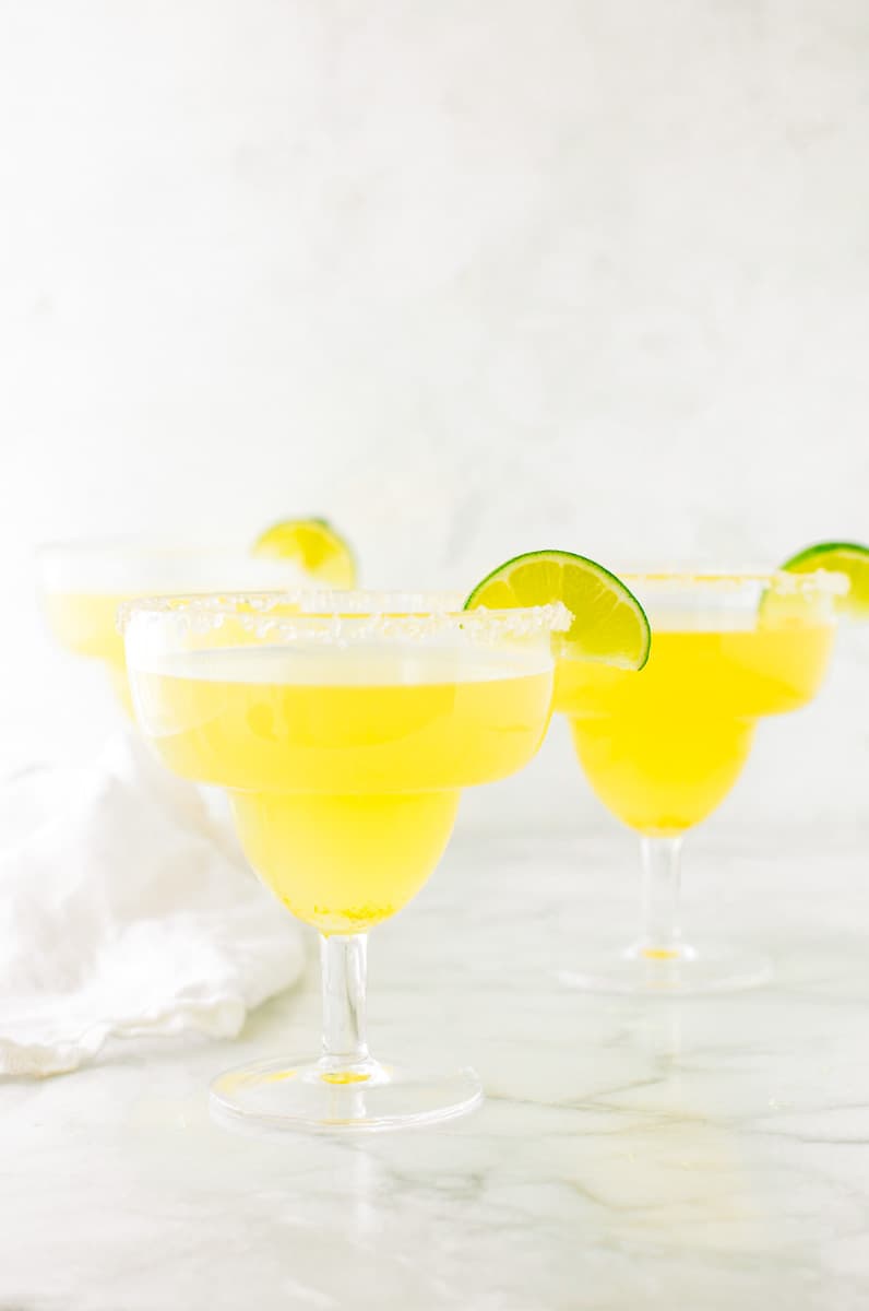 Three homemade margaritas in margarita glasses garnished with a wedge of lime and a salt rim.