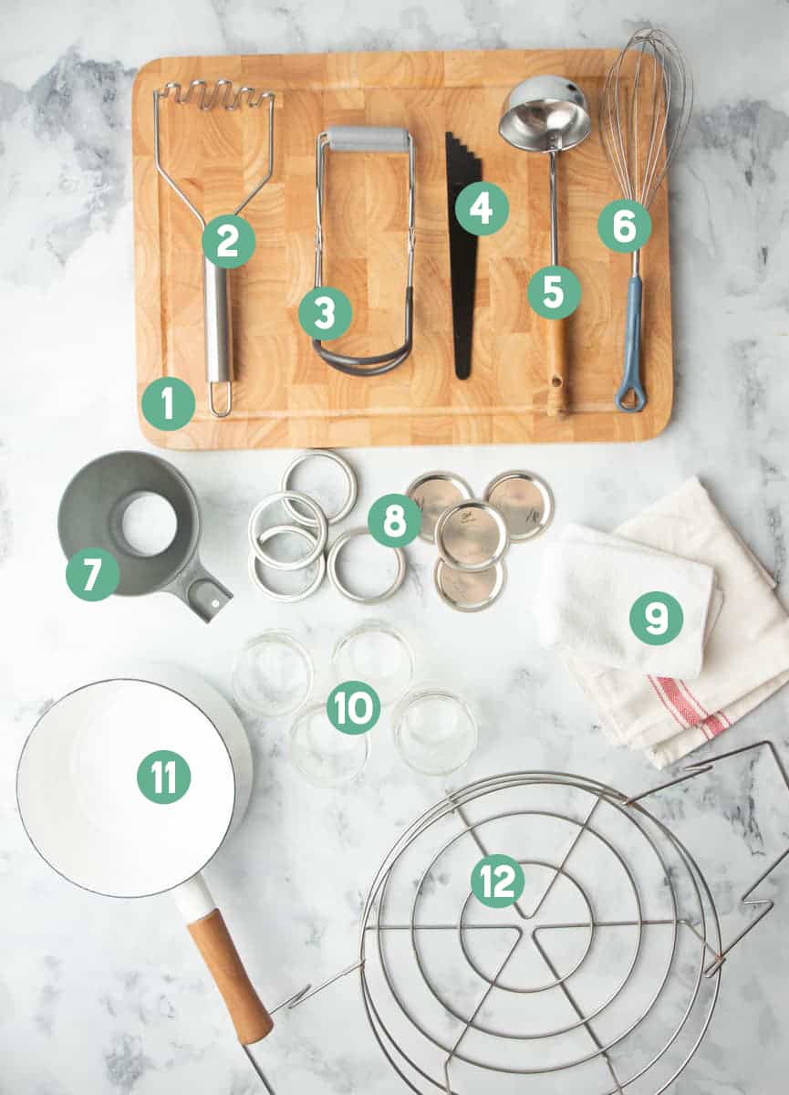 Tools for canning such as canning lids, ball jars, jar lifters, wide mouth funnel, laid out and numbered 1 through 12.