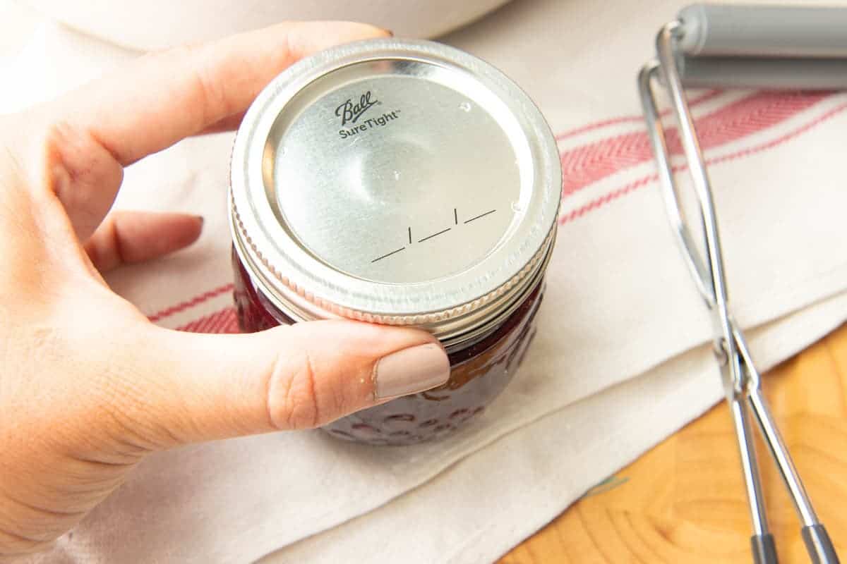 Close-up of hand tightening ring on full Ball jar of mixed berry agave jam.