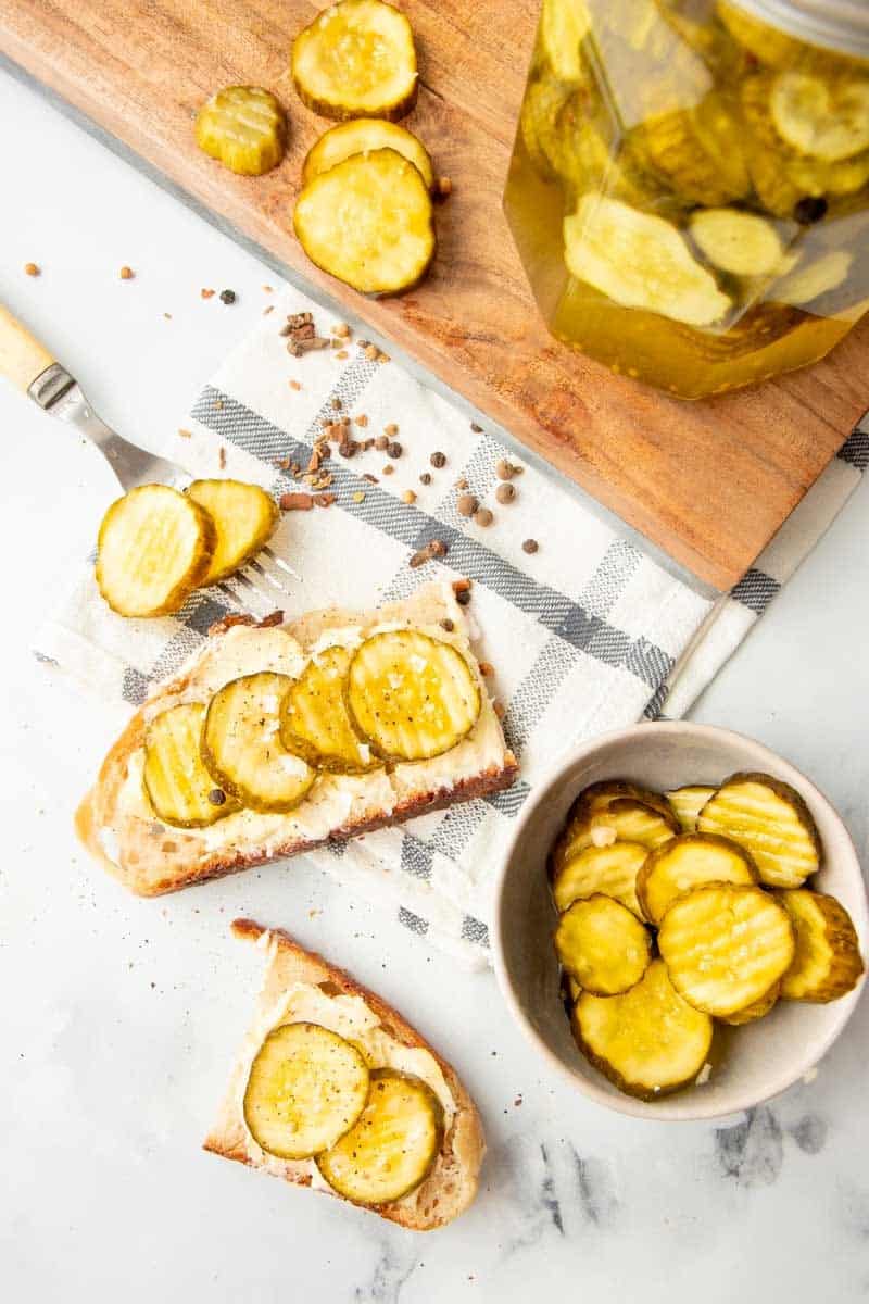 Overhead of bread and butter pickles on slice of buttered homemade sourdough bread.