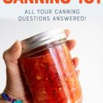 Close up of hand holding pint-sized mason jar of canned diced tomatoes. A text overlay reads, "Waterbath Canning 101, All Your Canning Questions Answered!"