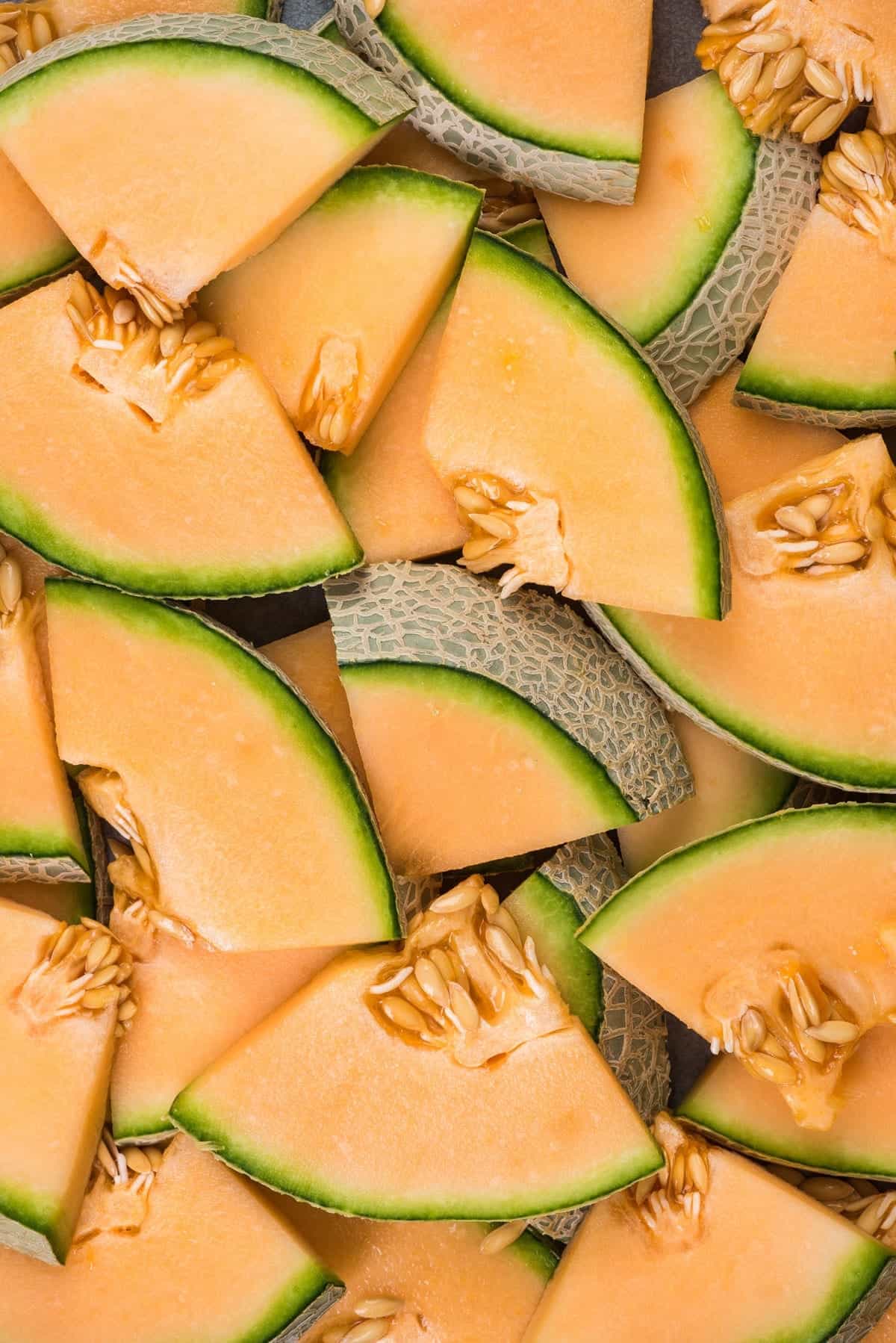 Overhead of cantaloupe circles sliced into quarters and lying flat in a colorful jumble.