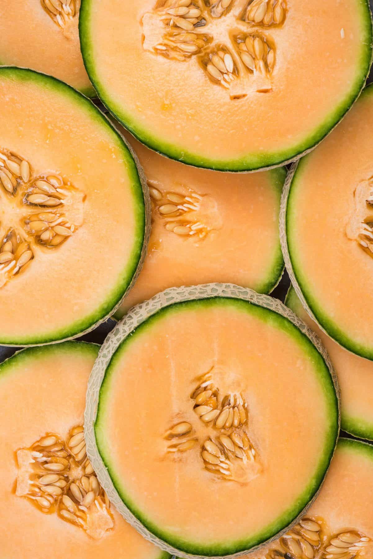 Overhead of full circle cantaloupe slices with their seeds stacked in two layers.
