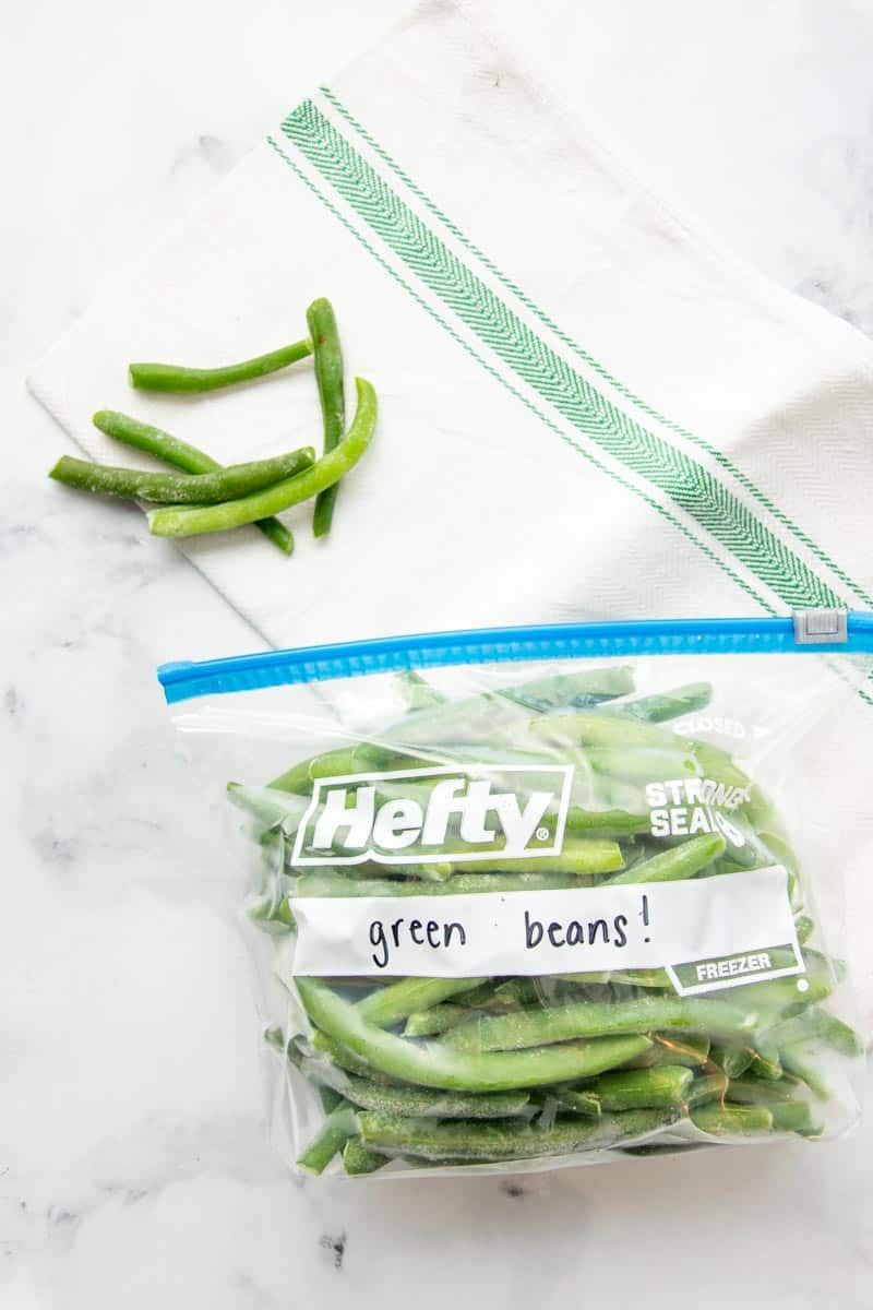 Overhead of Hefty freezer bag lying on its side, labeled and filled with individually frozen green beans.