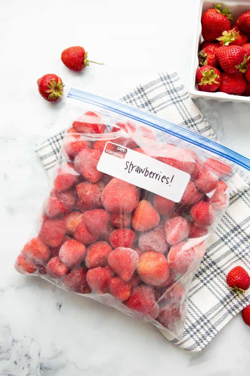 Freezer bag labeled strawberries lying on it's side, closed, and full of whole, hulled, individually frozen strawberries.