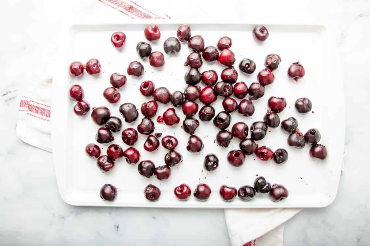Overhead of white baking sheet filled with a single layer of fresh, pitted cherries.
