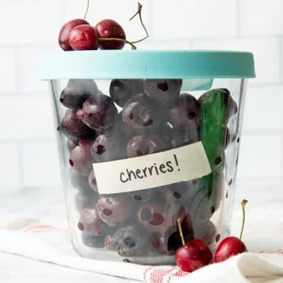 Tall glass container with lid, labeled and filled with individually frozen, pitted cherries.