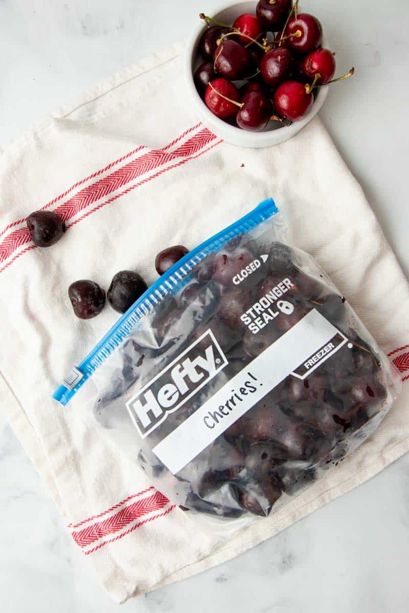 Overhead of open Hefty freezer bag lying on its side, filled with individually frozen, pitted cherries.
