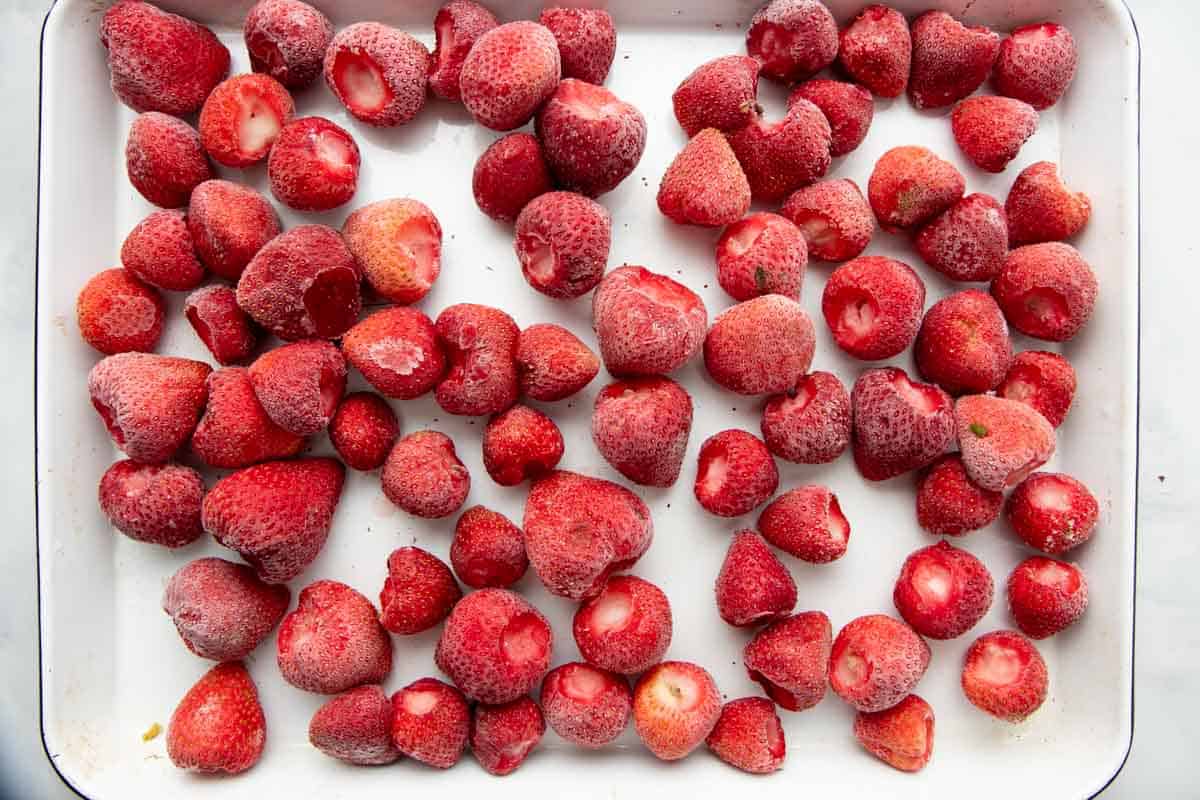 Overhead of whole, hulled, individually frozen strawberries on a baking sheet.
