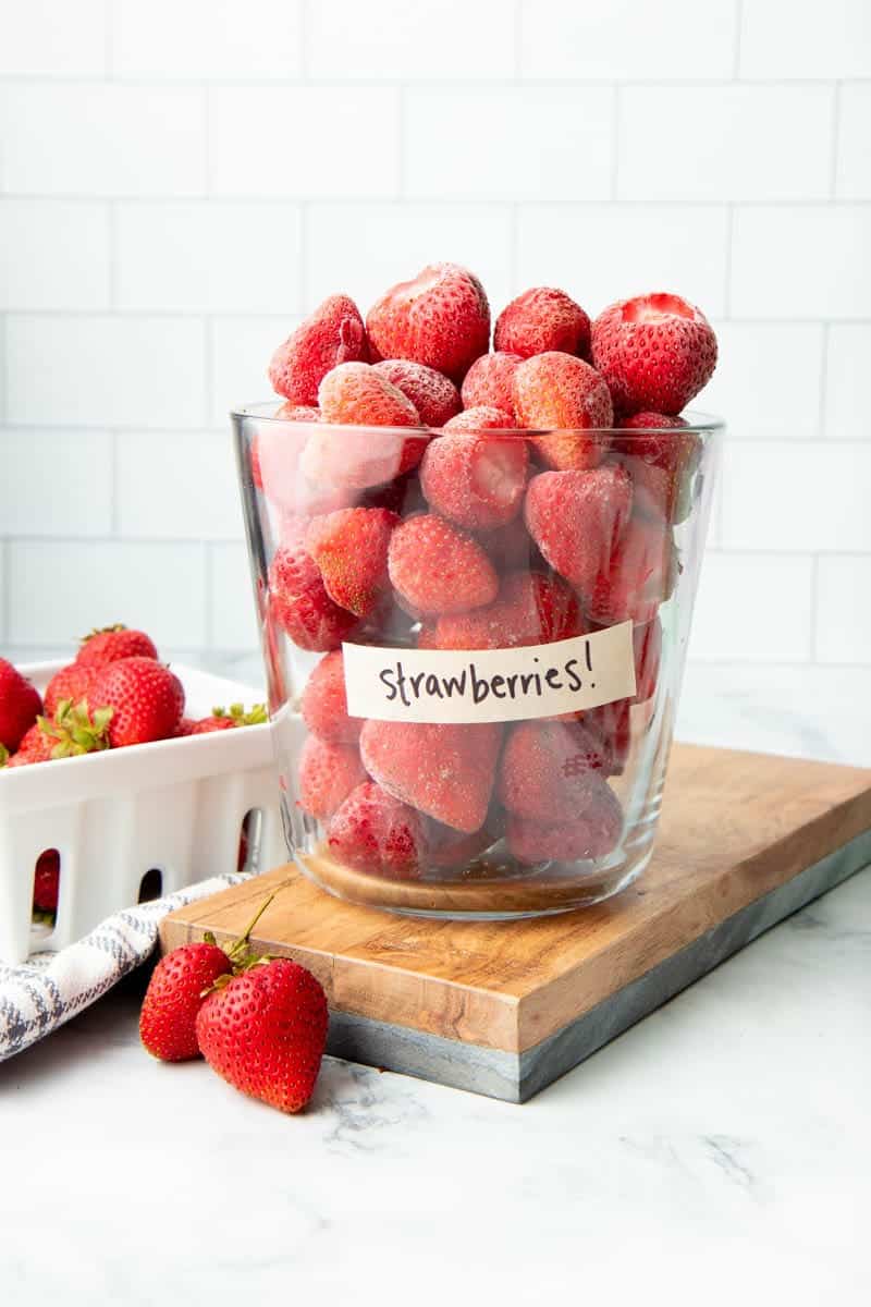 Frozen berries piled high in a glass container resting on a wooden cutting board.