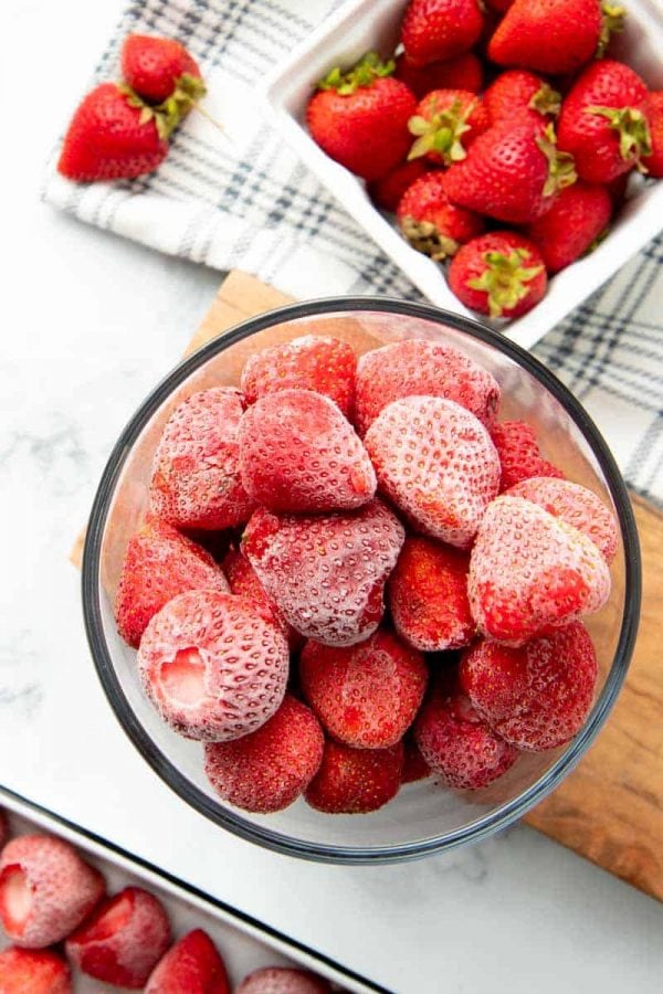 Overhead of whole, hulled, individually frozen strawberries in a glass container.