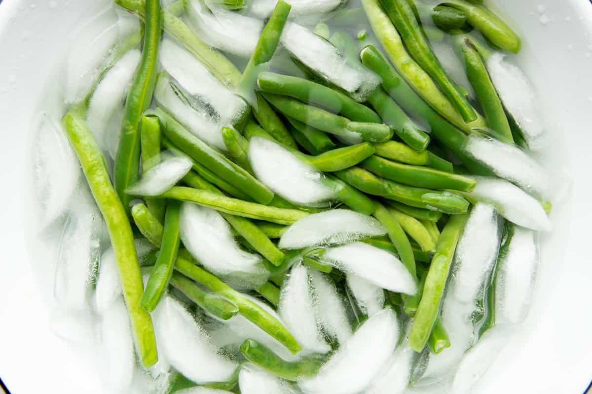 Overhead of blanched green beans in an ice bath.