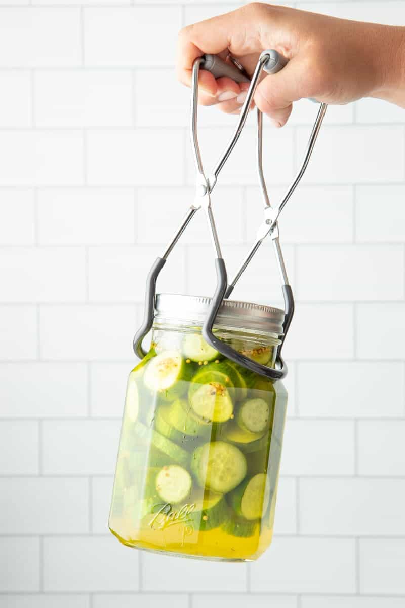 A jar lifter for water bath canning holds a jar of pickles.