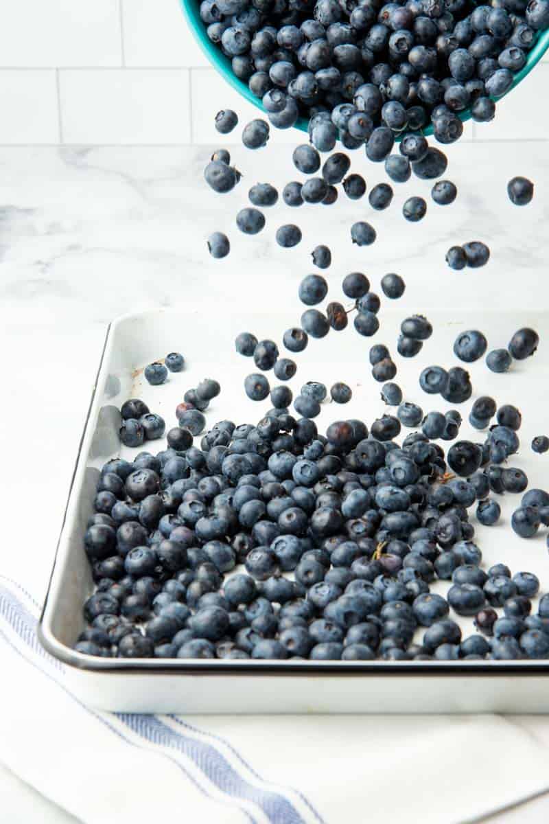 A bowl filled with fresh berries pours them out onto a baking sheet.