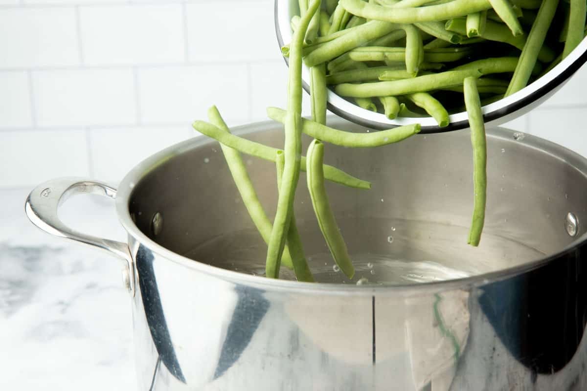 Fresh trimmed green beans in a bowl, tipping into a pot of boiling water.