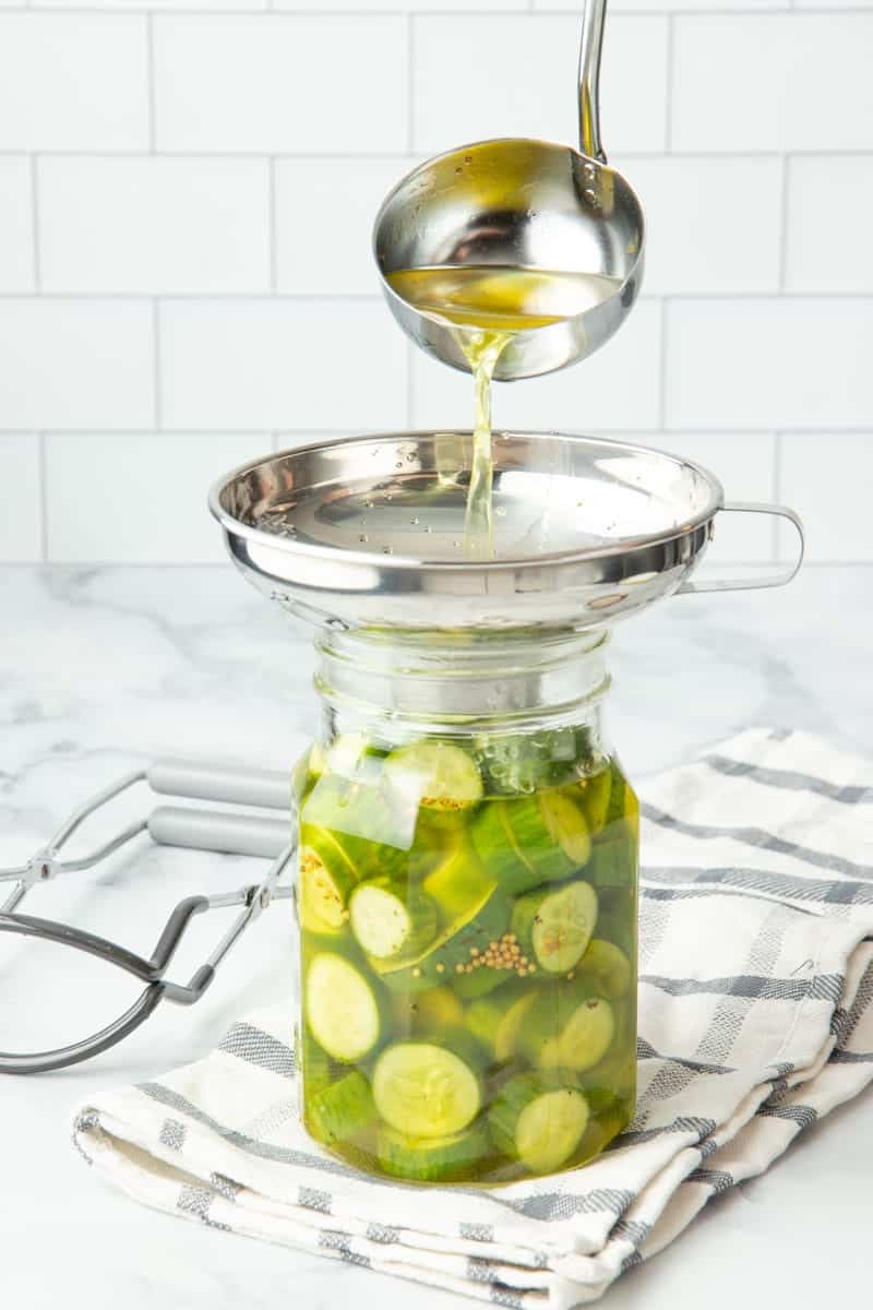 Pouring brine through a wide-mouth canning funnel into a jar of bread and butter pickles.