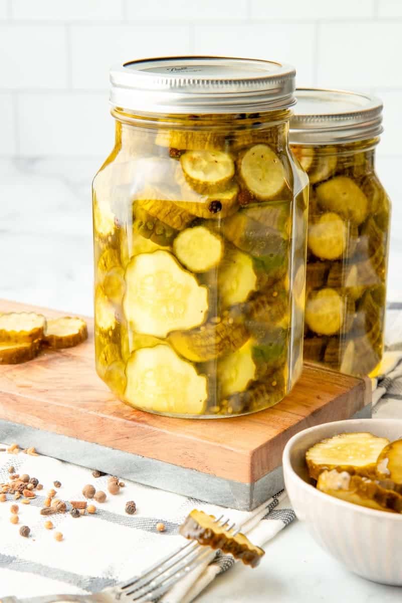 Two quart canning jars full of bread and butter pickles with finished pickles and spices.