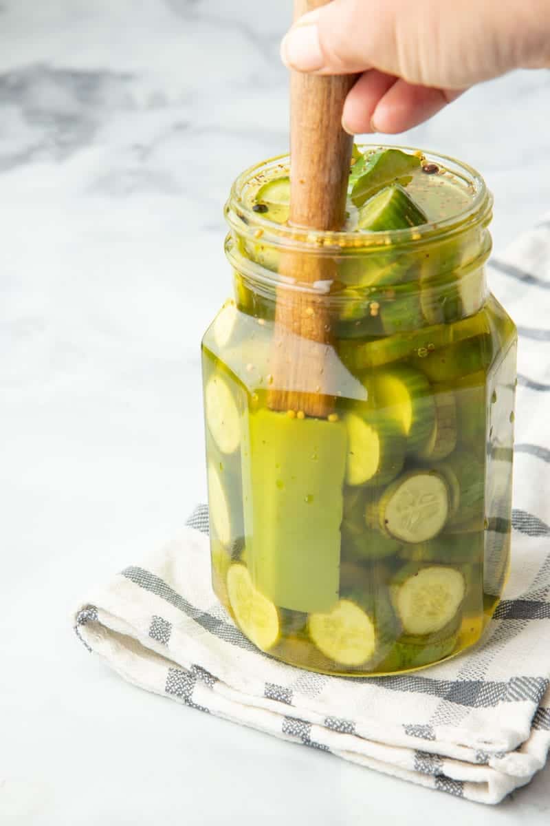 Close view of small spatula removing air bubbles from inside a jar of bread and butter pickles.