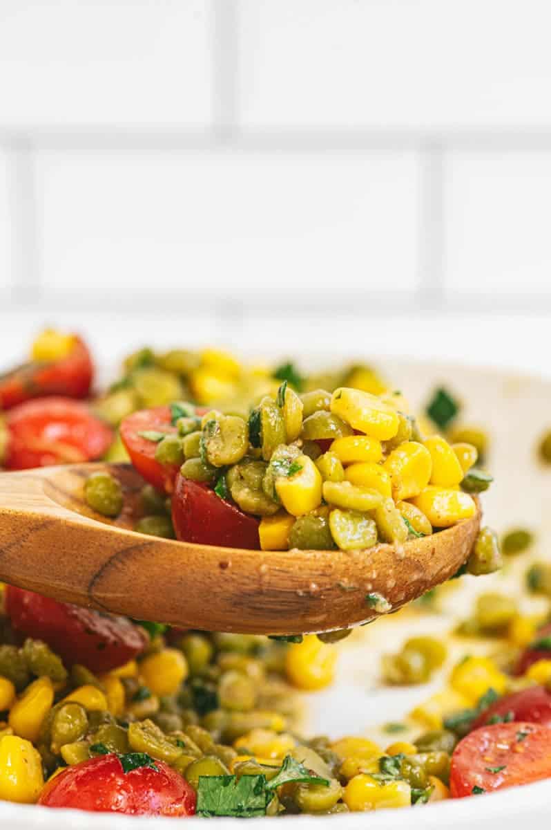 Close-up of wooden spoon with a big scoop of split pea salad over a serving bowl.