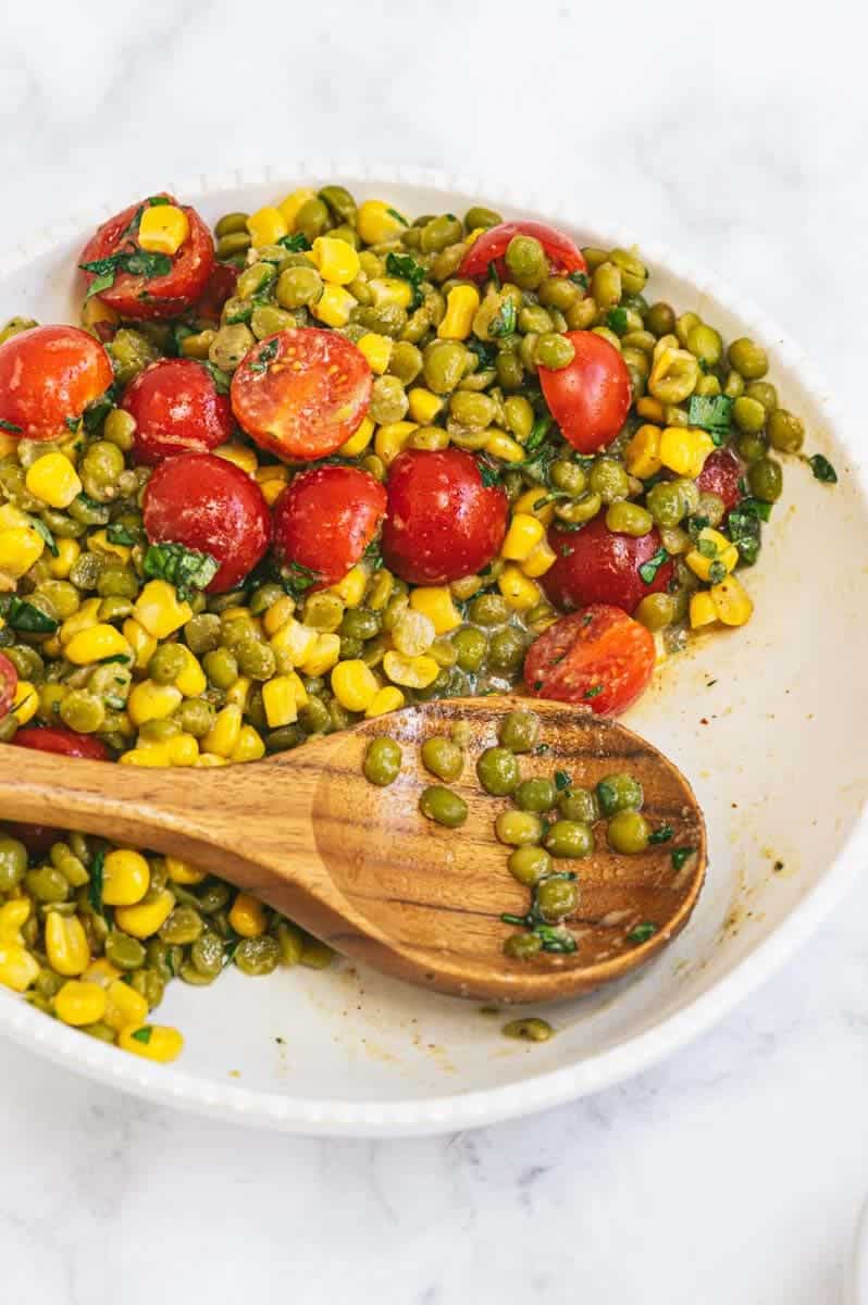 Close-up of serving bowl half-full of split pea salad and wooden serving spoon with split peas on it.