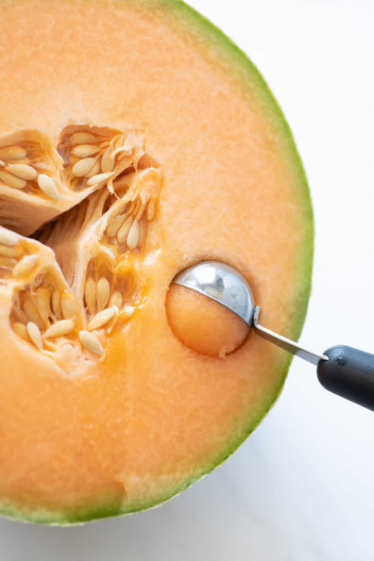 Close-up of melon baller scooping into the cut side of a cantaloupe half.