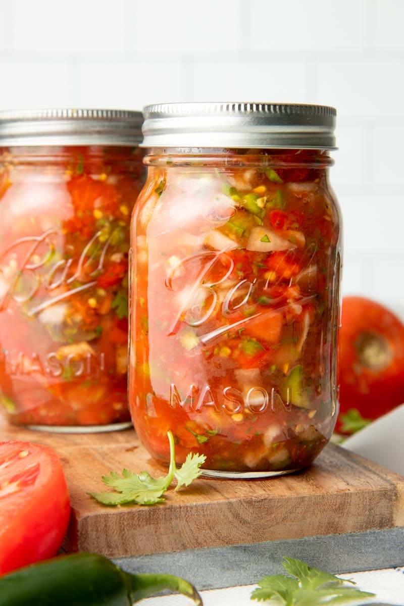 Close-up of canning salsa in mason jars on a cutting board.