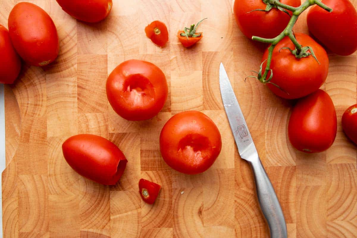 Overhead of three fresh tomatoes in the center of a wooden cutting board with their cores removed.