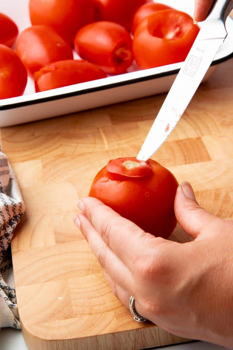 Close up of coring a tomato on a wooden cutting board.