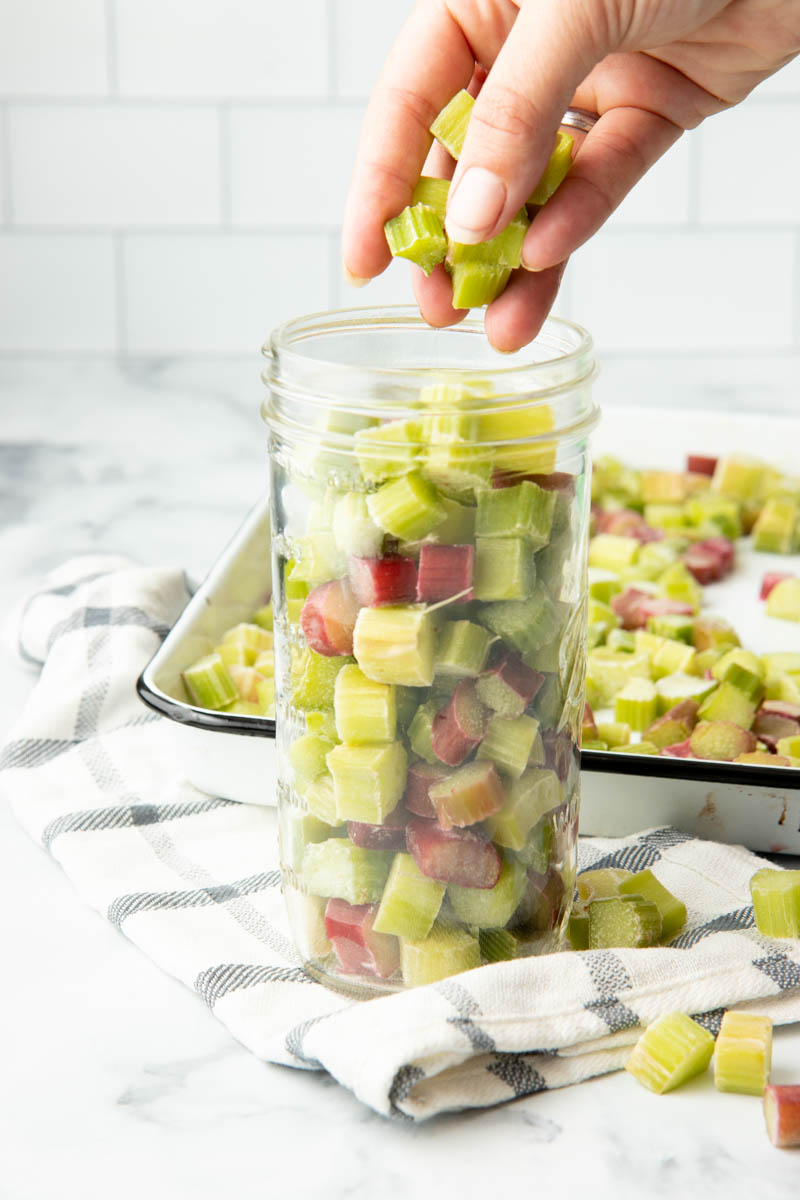 Close-up of filling a mason jar with individually frozen pieces of rhubarb by the handful.