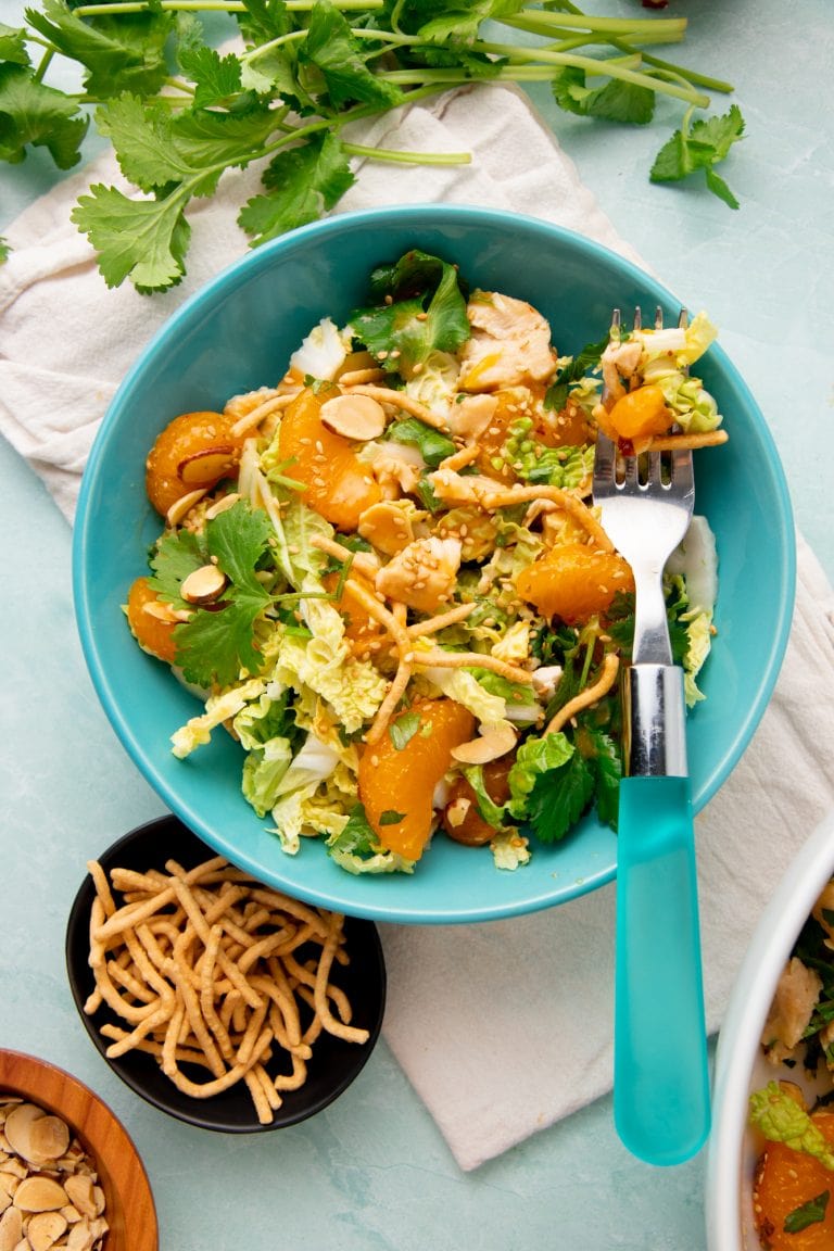 A forkful of mandarin chicken salad rests atop a single serving bowl of salad.