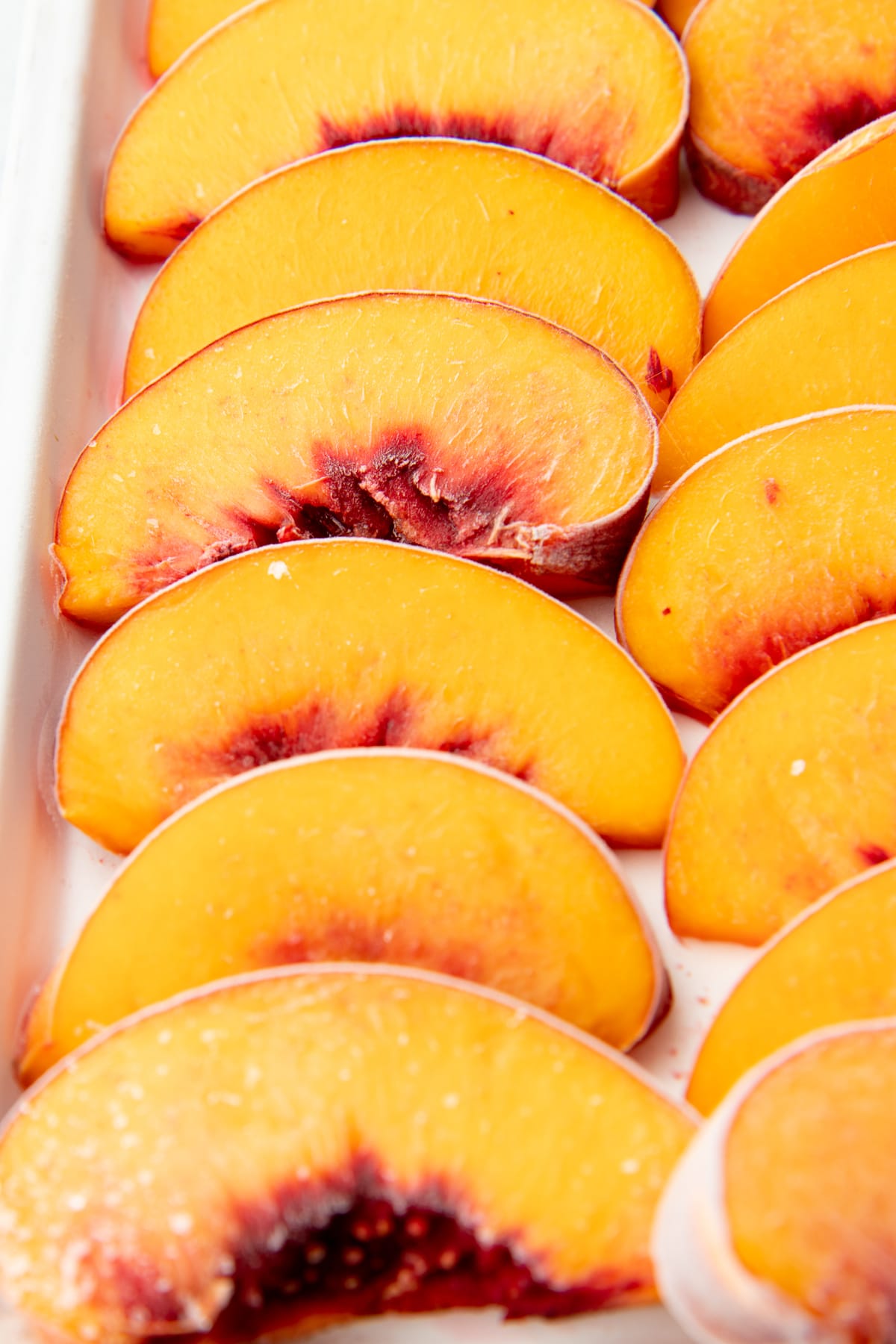 Close-up of individually frozen peach slices on a baking sheet.