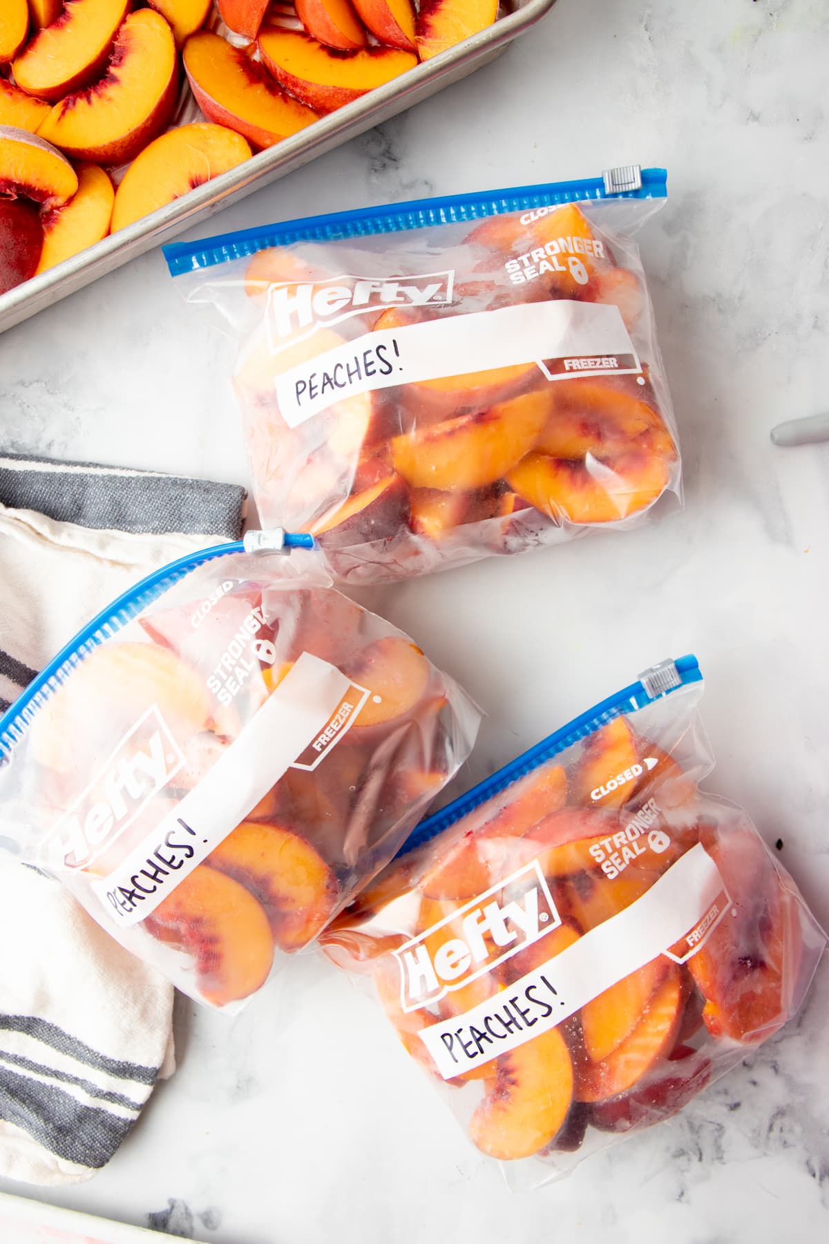 Overhead of three freezer bags filled with individually frozen peach slices lying on their sides. The bags are labeled "Peaches!"