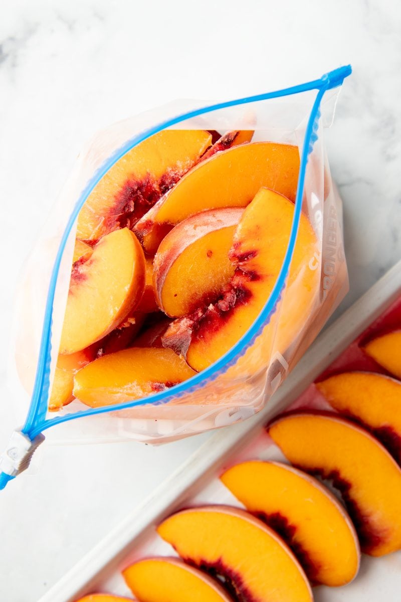 Overhead of open freezer bag filled with individually frozen peach slices.