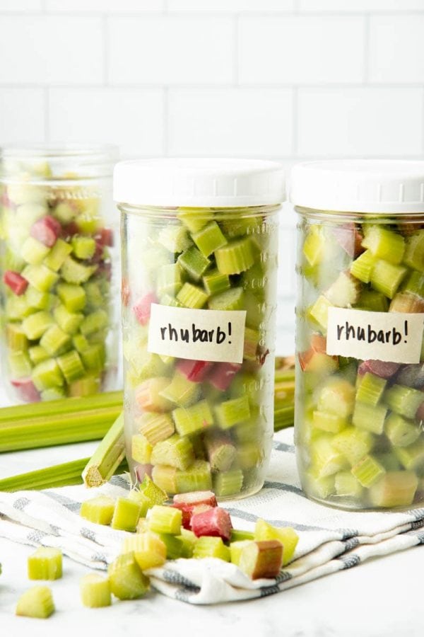 Three jars filled with individually frozen pieces of cut rhubarb standing on a kitchen towel.