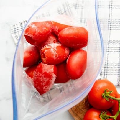 Overhead of open zip-lock freezer bag filled with cored and individually frozen tomatoes.