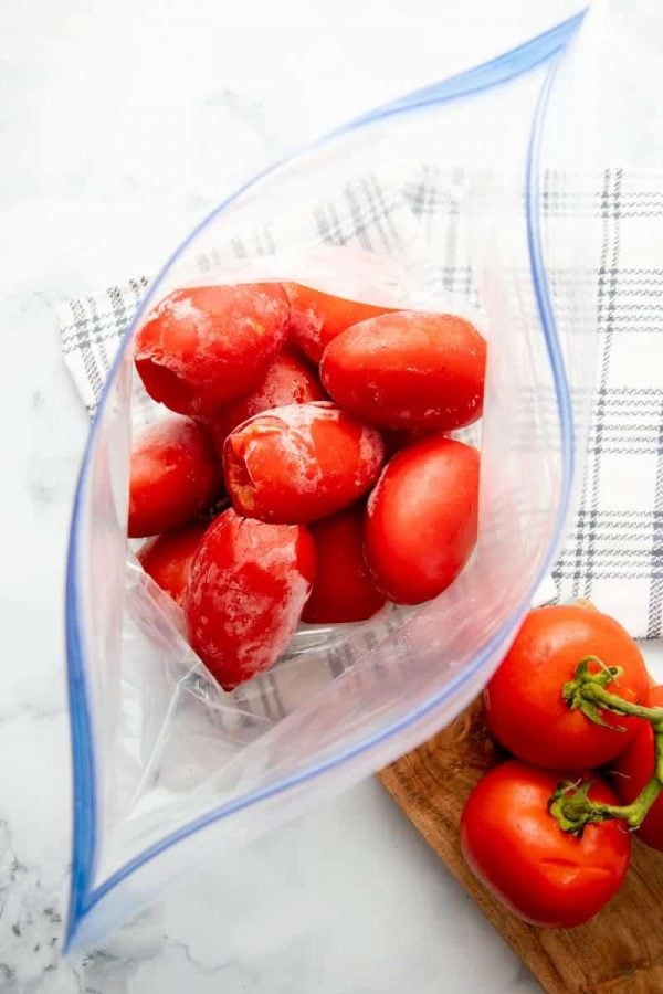 Overhead of open zip-lock freezer bag filled with cored and individually frozen tomatoes.