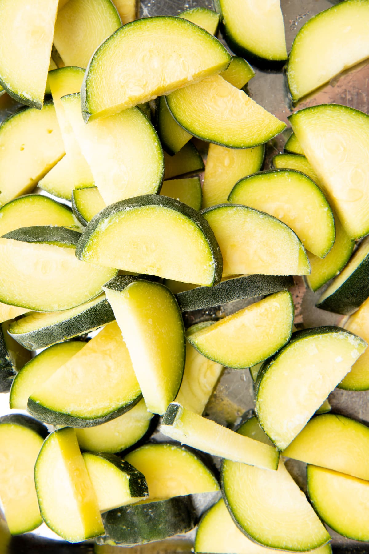 Close-up of individually frozen zucchini slices on a baking sheet.