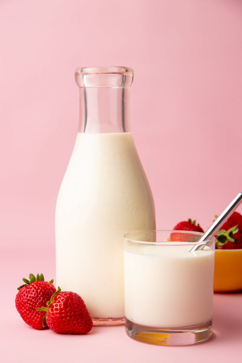 Close-up of a glass carafe and glass tumbler full of homemade kefir with ripe, red strawberries alongside.
