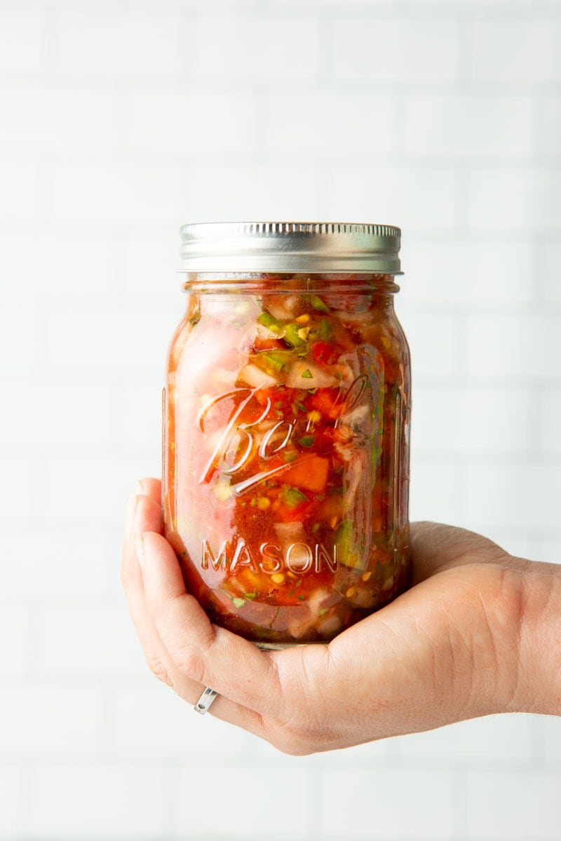 Close-up of a jar of salsa cupped into the palm of someone's hand.