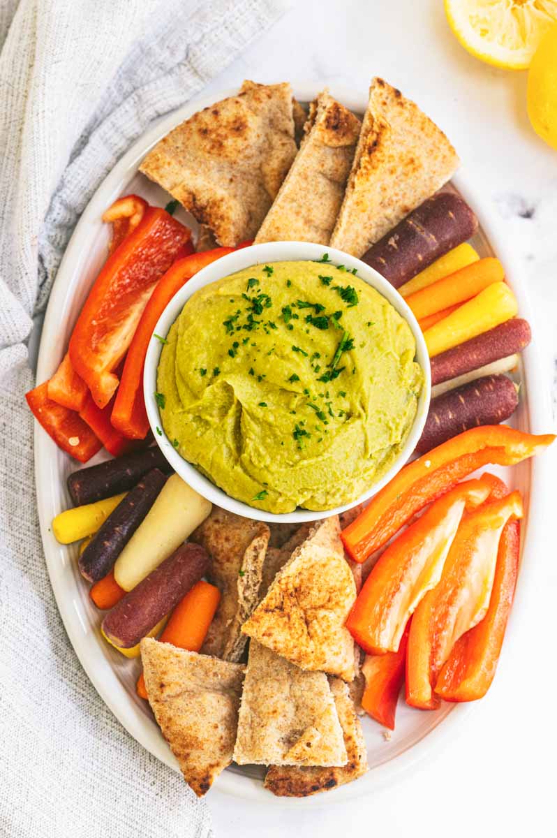 Overhead of a party platter of split pea hummus with veggies and pita chips for dipping.