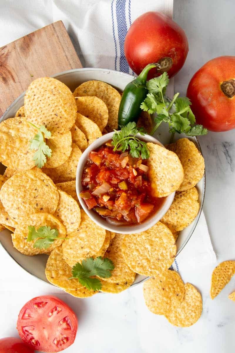 Overhead of a platter of tortilla chips with a bowl of zesty salsa nestled among the chips.