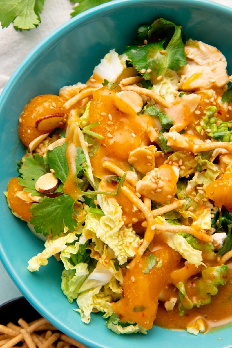 Close-up of a single serving of mandarin chicken salad in a bowl with dressing on top.