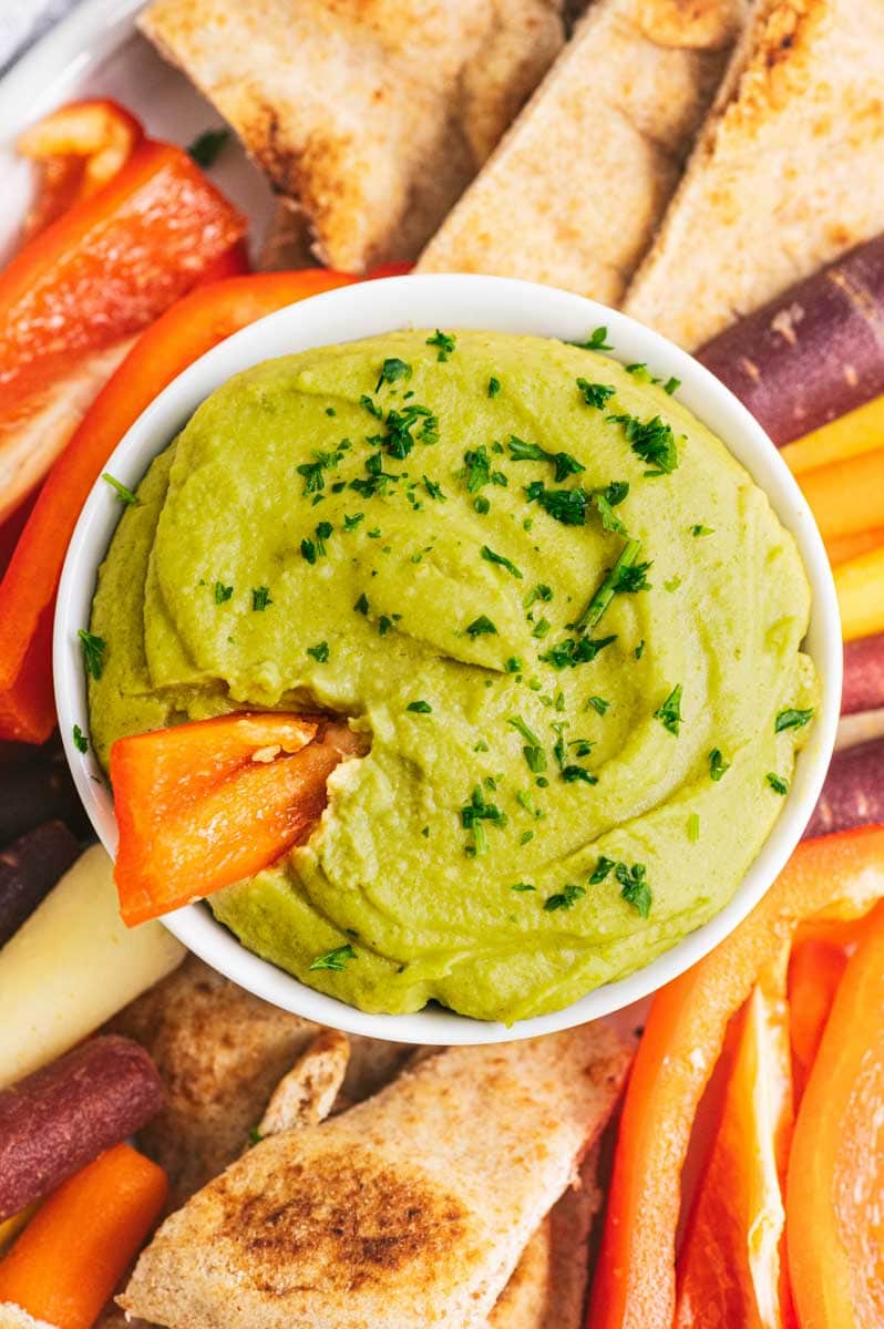 Close-up of a bowl of finished split pea hummus with a red bell pepper strip dipped into it.